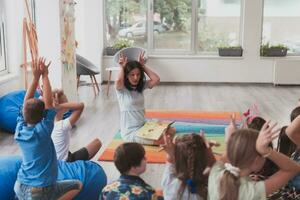 A happy female teacher sitting and playing hand games with a group of little schoolchildren photo