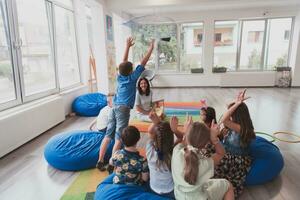 A happy female teacher sitting and playing hand games with a group of little schoolchildren photo