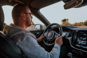 un hombre con un Gafas de sol conducción un coche a puesta de sol. el concepto de coche viaje foto