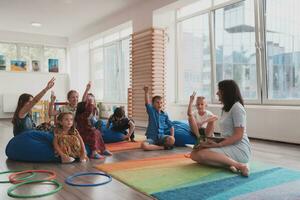 A happy female teacher sitting and playing hand games with a group of little schoolchildren photo