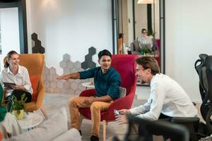 Multiethnic startup business team having brainstorming in relaxation area of modern office interior working on laptop and tablet computer photo