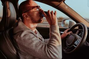 A tired man drinking acoffee while driving a car at sunset. Tired travel and long drive photo