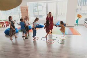 Small nursery school children with female teacher on floor indoors in classroom, doing exercise. Jumping over hula hoop circles track on the floor. photo