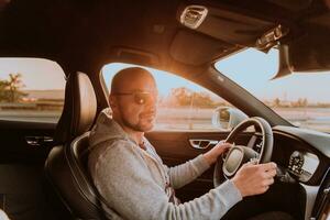 un hombre con un Gafas de sol conducción un coche a puesta de sol. el concepto de coche viaje foto