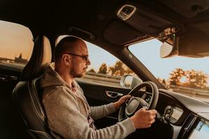 un hombre con un Gafas de sol conducción un coche a puesta de sol. el concepto de coche viaje foto