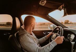 un hombre con un Gafas de sol conducción un coche a puesta de sol. el concepto de coche viaje foto