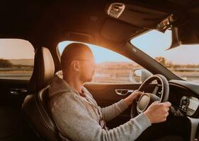 un hombre con un Gafas de sol conducción un coche a puesta de sol. el concepto de coche viaje foto