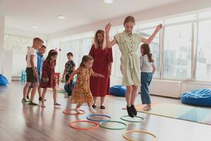 Small nursery school children with female teacher on floor indoors in classroom, doing exercise. Jumping over hula hoop circles track on the floor. photo