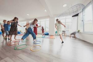 Small nursery school children with female teacher on floor indoors in classroom, doing exercise. Jumping over hula hoop circles track on the floor. photo