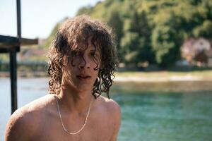 Portrait of a young teen boy with curly wet hair near the river having fun with friends at a summer party. photo