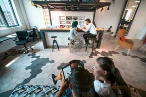 Group of casual multiethnic business people taking break from the work doing different things while enjoying free time in relaxation area at modern open plan startup office photo