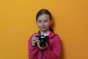 Little girl photographer isolated on yellow background smiling taking photos with a retro vintage camera.