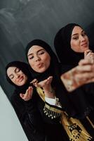 grupo de joven hermosa musulmán mujer en de moda vestir con hijab utilizando teléfono inteligente mientras tomando selfie imagen en frente de negro antecedentes foto