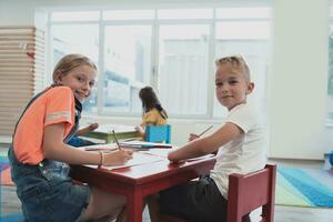 linda niña y chico sentar y dibujar juntos en preescolar institución foto