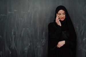 joven moderno musulmán negocio mujer utilizando teléfono inteligente vistiendo hijab ropa en frente de negro pizarra foto
