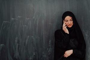 Young modern muslim business woman using smartphone wearing hijab clothes in front of black chalkboard photo