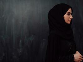 Portrait of beautiful muslim woman in fashionable dress with hijab in front of black chalkboard representing modern islam fashion and ramadan kareem concept photo