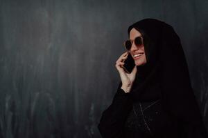 Young modern muslim business woman using smartphone wearing hijab clothes in front of black chalkboard photo