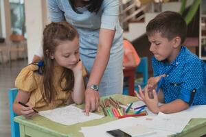 Creative kids during an art class in a daycare center or elementary school classroom drawing with female teacher. photo