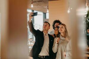 Group of cheerful colleagues taking selfie and gesturing while standing in the modern office. photo