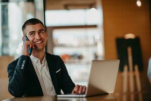 Happy business man sitting at cafeteria with laptop and smartphone photo