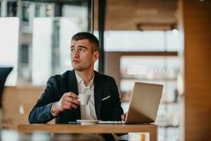 Happy business man sitting at cafeteria with laptop and smartphone photo