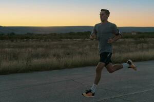 atractivo ajuste hombre corriendo rápido a lo largo campo la carretera a puesta de sol luz, haciendo trotar rutina de ejercicio al aire libre foto