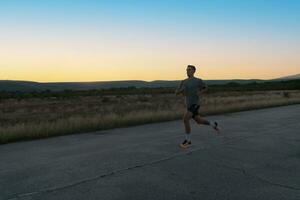 Attractive fit man running fast along countryside road at sunset light, doing jogging workout outdoors photo