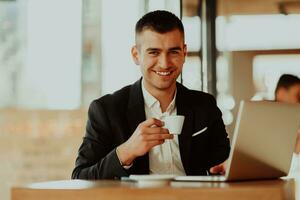 Happy business man sitting at cafeteria with laptop and smartphone photo