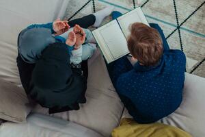 Traditional muslim family parents with children reading Quran and praying together on the sofa before iftar dinner during a ramadan feast at home top view photo