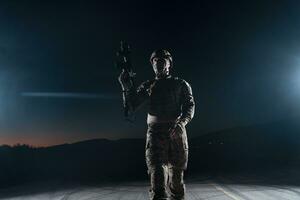 Army soldier in Combat Uniforms with an assault rifle, plate carrier and combat helmet going on a dangerous mission on a rainy night. photo