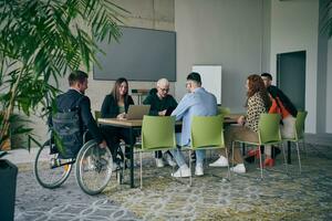 un diverso grupo de negocio profesionales, incluso un persona con un discapacidad, reunido a un moderno oficina para un productivo y inclusivo reunión. foto