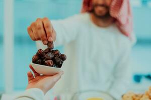 moderno multiétnico musulmán familia compartiendo un cuenco de fechas mientras disfrutando iftar cena juntos durante un Ramadán banquete a hogar foto