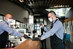 waiter in a medical protective mask serves  the coffee in restaurant photo