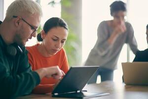 A young entrepreneurial couple sits together in a large, modern office, engaged in analyzing statistics and data on their laptop photo