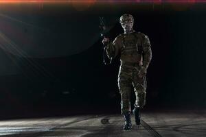 Army soldier in Combat Uniforms with an assault rifle, plate carrier and combat helmet going on a dangerous mission on a rainy night. photo