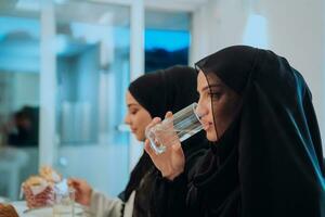 eid Mubarak musulmán familia teniendo iftar cena Bebiendo agua a descanso banquete. comiendo tradicional comida durante Ramadán banquete mes a hogar. el islámico halal comiendo y Bebiendo a moderno occidental isla foto