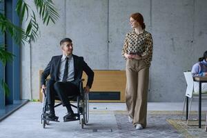 A businessman in a wheelchair and his female colleague together in a modern office, representing the power of teamwork, inclusion and support, fostering a dynamic and inclusive work environment. photo