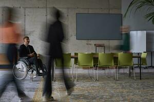 A businessman in a wheelchair in a modern office, surrounded by his colleagues who are portrayed with blurred movements, symbolizing their support and solidarity as they navigate the workspace together. photo