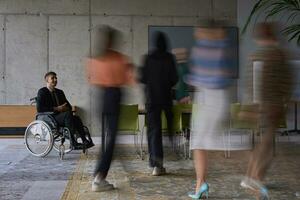 A businessman in a wheelchair in a modern office, surrounded by his colleagues who are portrayed with blurred movements, symbolizing their support and solidarity as they navigate the workspace together. photo