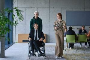 A group of business colleagues in a modern office exemplifies inclusivity and support as they compassionately wheel their business friend in a wheelchair, showcasing teamwork and empowerment in the workplace. photo