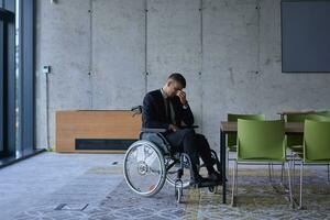 A melancholic businessman in a wheelchair sitting with a sad expression, gazing through the window of a modern office, conveying a sense of solitude photo