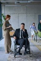 A businessman in a wheelchair and his female colleague together in a modern office, representing the power of teamwork, inclusion and support, fostering a dynamic and inclusive work environment. photo