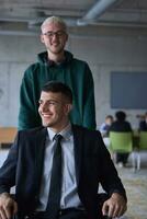 A young entrepreneur and his colleague, who is a person with a disability, fun together through a large, modern office, demonstrating the power of teamwork, inclusivity, and determination as they drive the wheelchair photo