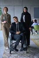 A businessman with disability in a wheelchair is surrounded by supportive colleagues in a modern office, showcasing the strength of teamwork, inclusivity, and empowerment in the face of challenges. photo