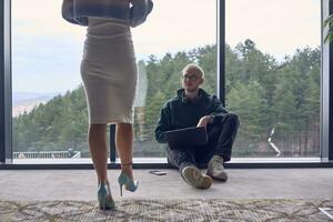 A young blond man in a modern office is sitting by the window, engrossed in his work on a laptop while talking to a female colleague photo