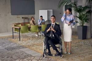 A businessman in a wheelchair and his female colleague together in a modern office, representing the power of teamwork, inclusion and support, fostering a dynamic and inclusive work environment. photo