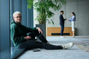 A young blond man in a modern office sits by the window, engrossed in his work on a laptop photo