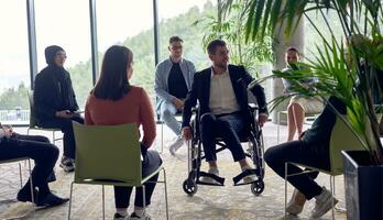 un empresario en un silla de ruedas en el centrar de el círculo, apasionadamente compartiendo su negocio ideas con su colegas, Fomentando un atmósfera de colaboración y innovación en un dinámica y atractivo lugar de trabajo. foto