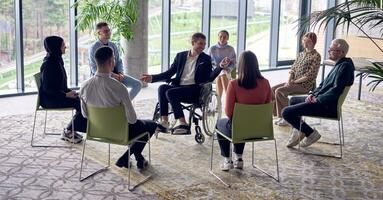 un empresario en un silla de ruedas en el centrar de el círculo, apasionadamente compartiendo su negocio ideas con su colegas, Fomentando un atmósfera de colaboración y innovación en un dinámica y atractivo lugar de trabajo. foto